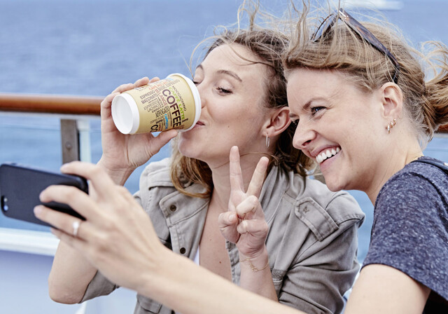 To kvinder på færgens soldæk drikker kaffe og tager selfie